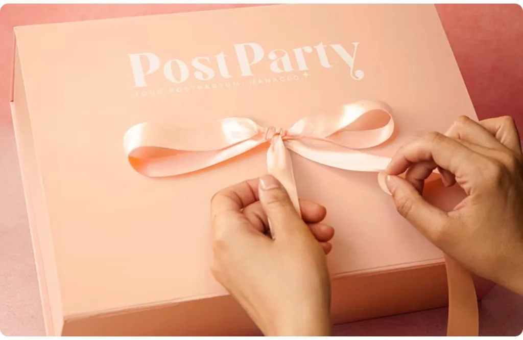 Hands untying a pink ribbon on a peach PostParty box.