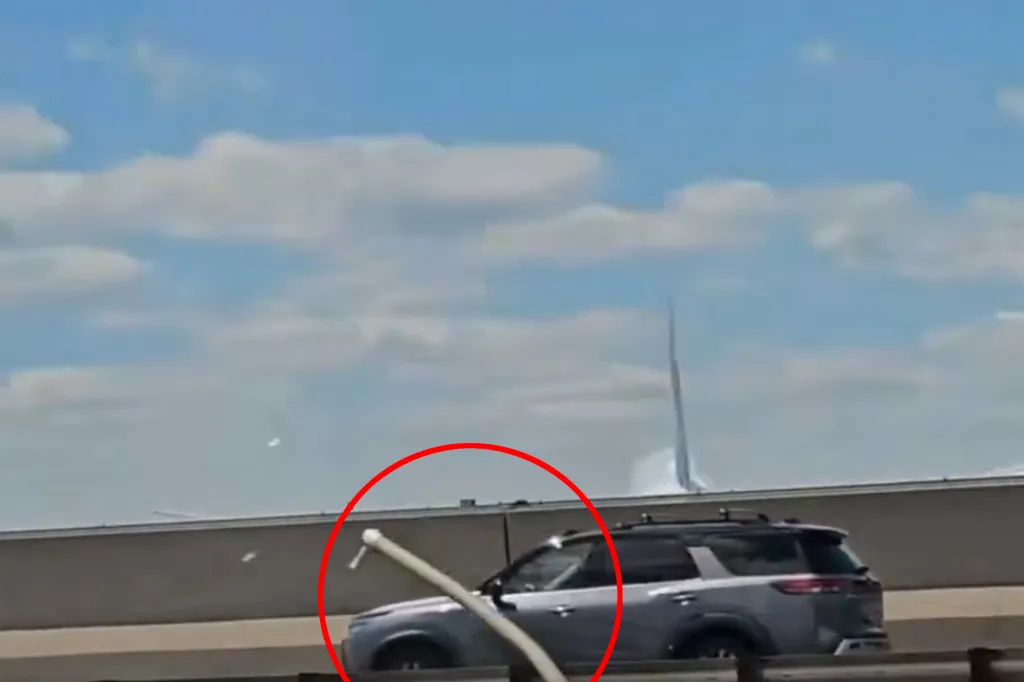 A red circle highlights a light pole that has fallen onto the roof of a gray SUV on a highway.