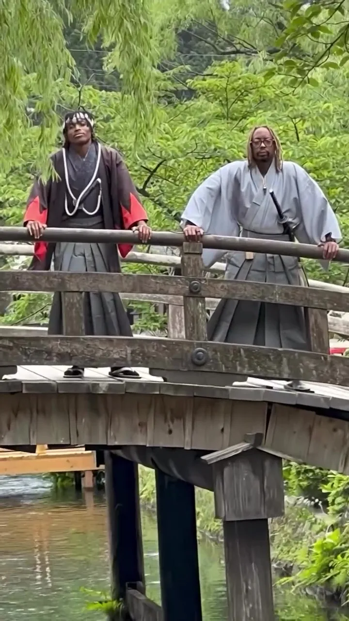 Lil Jon and his son, Nathan, dressed in traditional Japanese clothing on a wooden bridge over water.