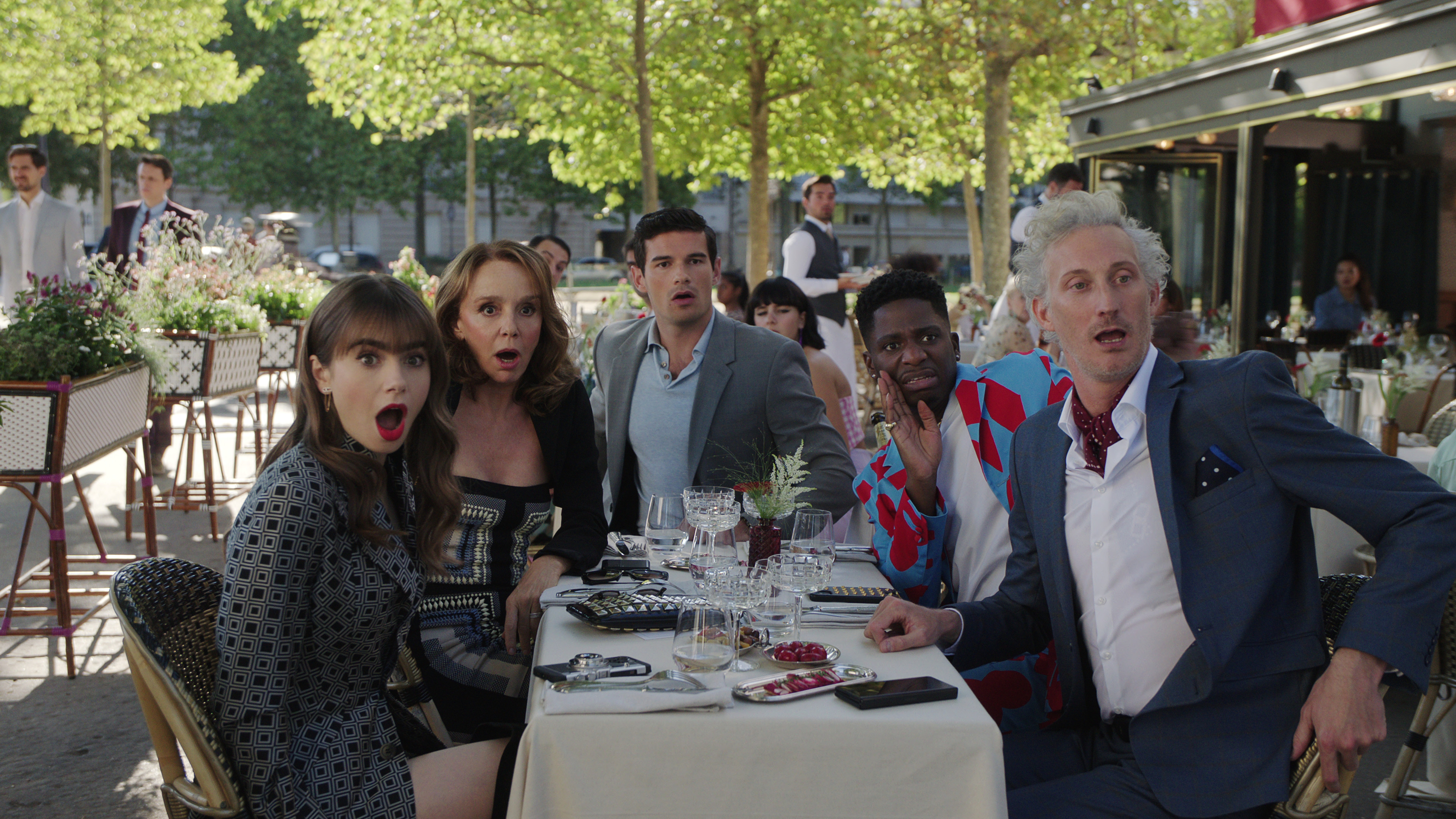 Emily in Paris cast members Emily, Sylvie, Nicolas, Julien, and Luc reacting with surprise at an outdoor café.