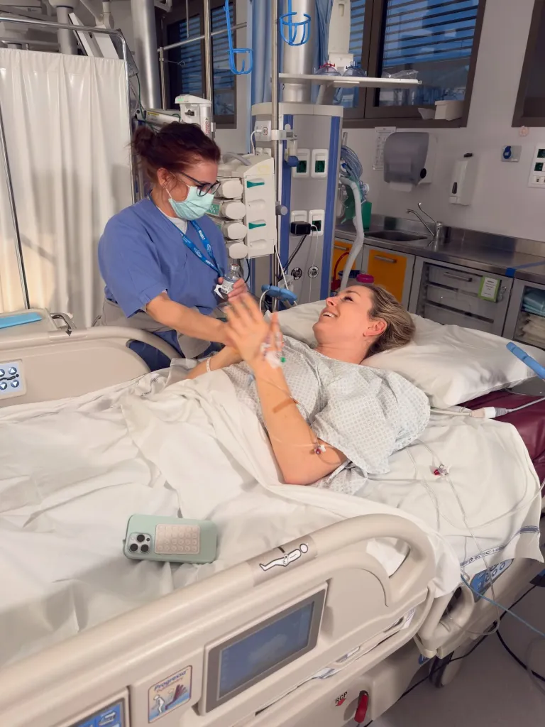 Lindsey Vonn in a hospital bed in Italy, smiling at a masked nurse.