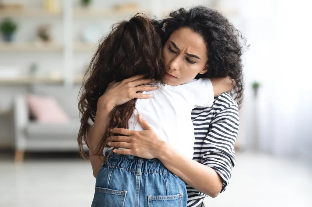 A mother comforts her crying daughter with a hug.