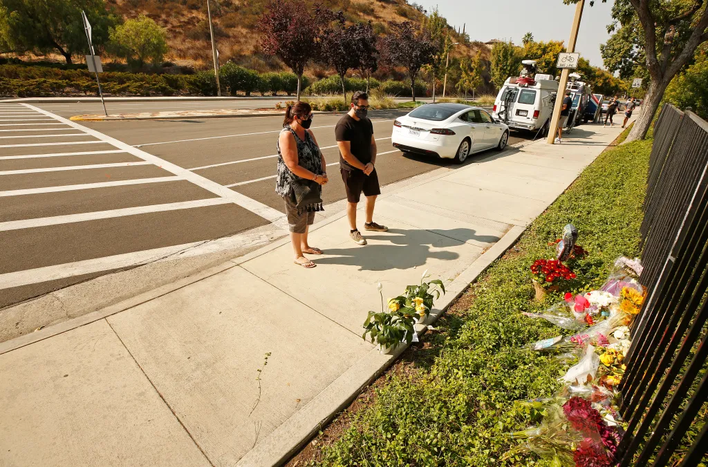 Lorraine Maralian and her son Anthony Maralian stand on a sidewalk, placing flowers and praying at a growing memorial in Westlake Village.