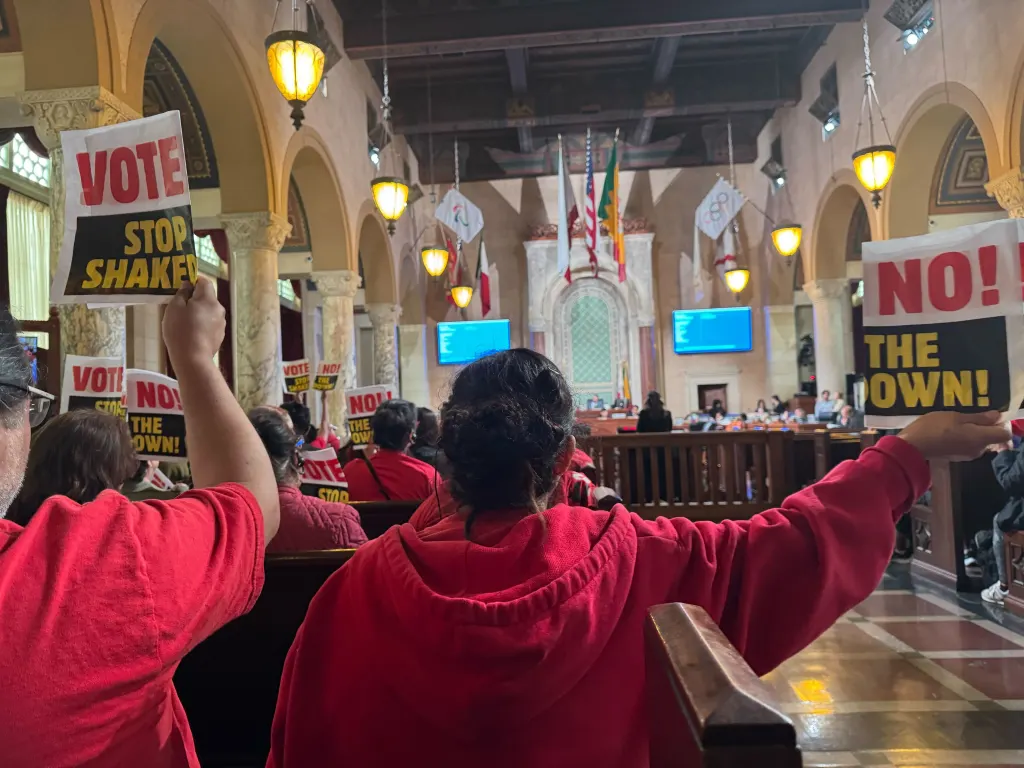 People in red shirts hold signs protesting a minimum wage hike at Los Angeles City Hall.
