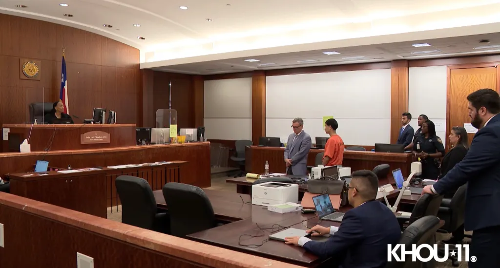 Raudel Orozo in an orange jumpsuit standing next to his lawyer in a courtroom.