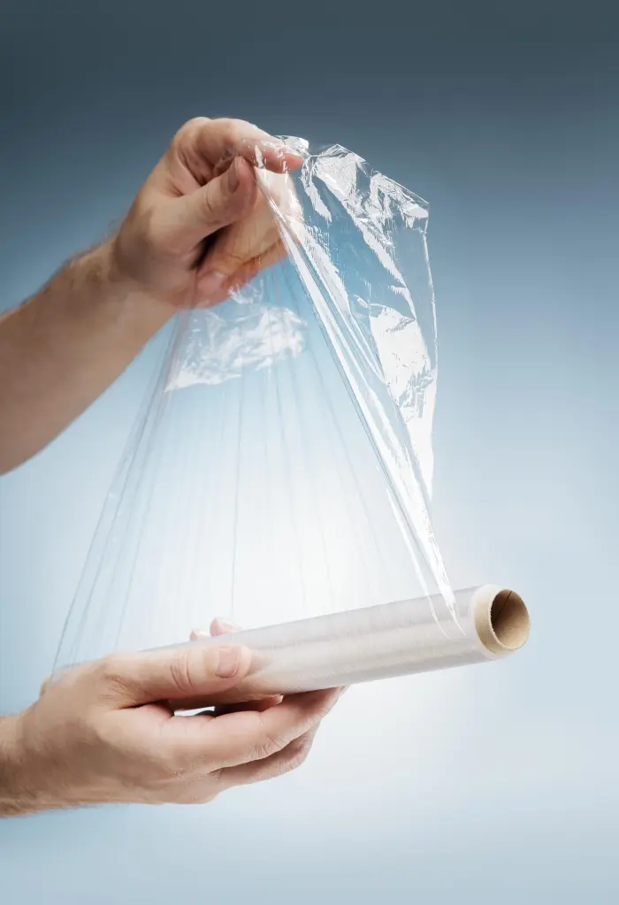 Hands pulling plastic film from a roll.