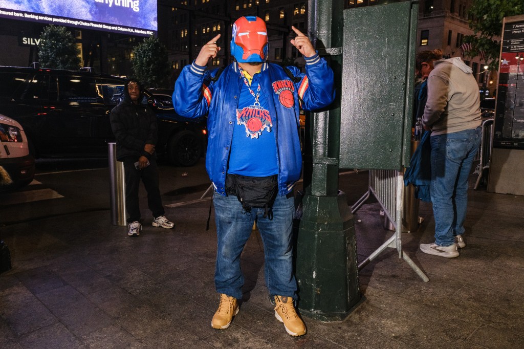 Marcus Nartatez wears a Knicks Iron Man helmet and a blue Knicks jacket, gesturing with both hands.