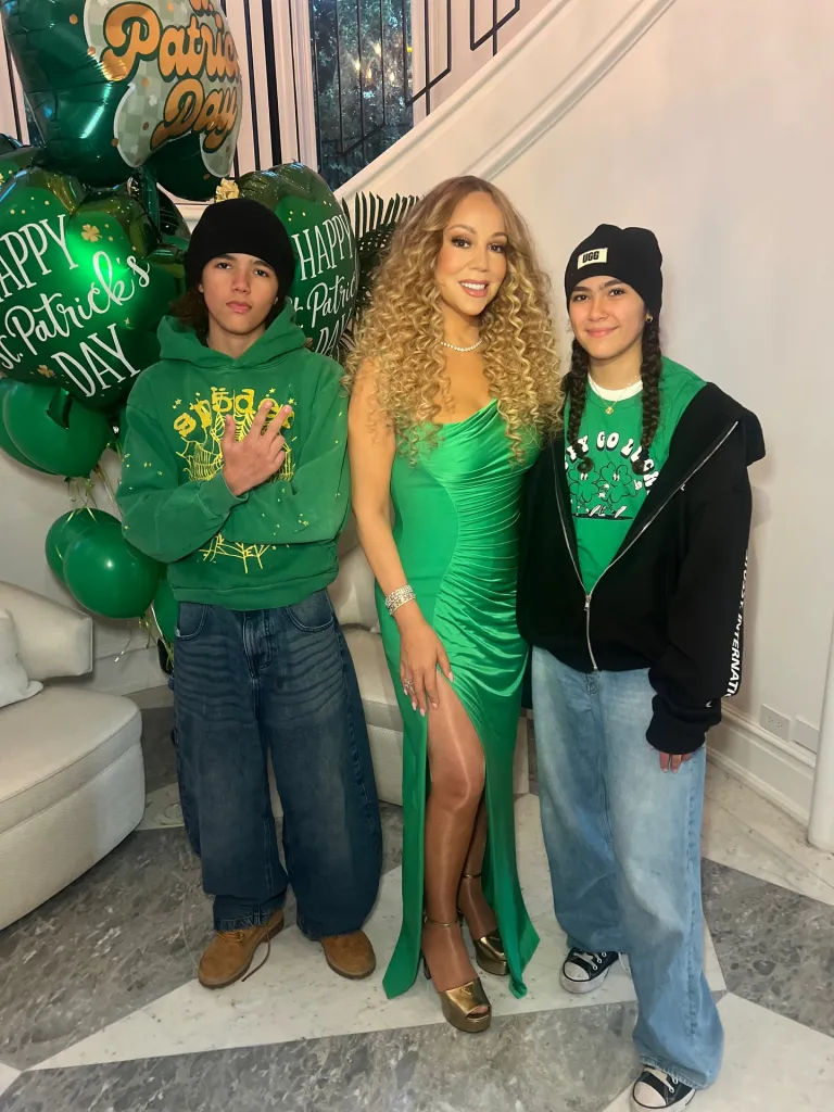 Mariah Carey and her two children standing in a room with St. Patrick's Day decorations.