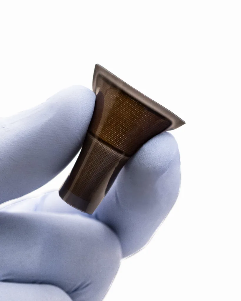 Hand in a blue glove holding a brown wearable ultrasound patch.