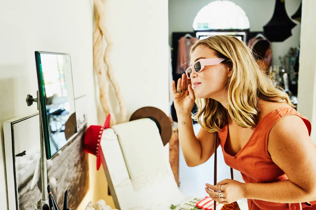 Smiling woman trying on pink sunglasses while shopping in a boutique.