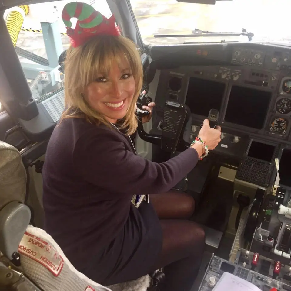 Meesh Carpino, a flight attendant for Southwest Airlines, smiling in a pilot's seat with a holiday elf hat on.
