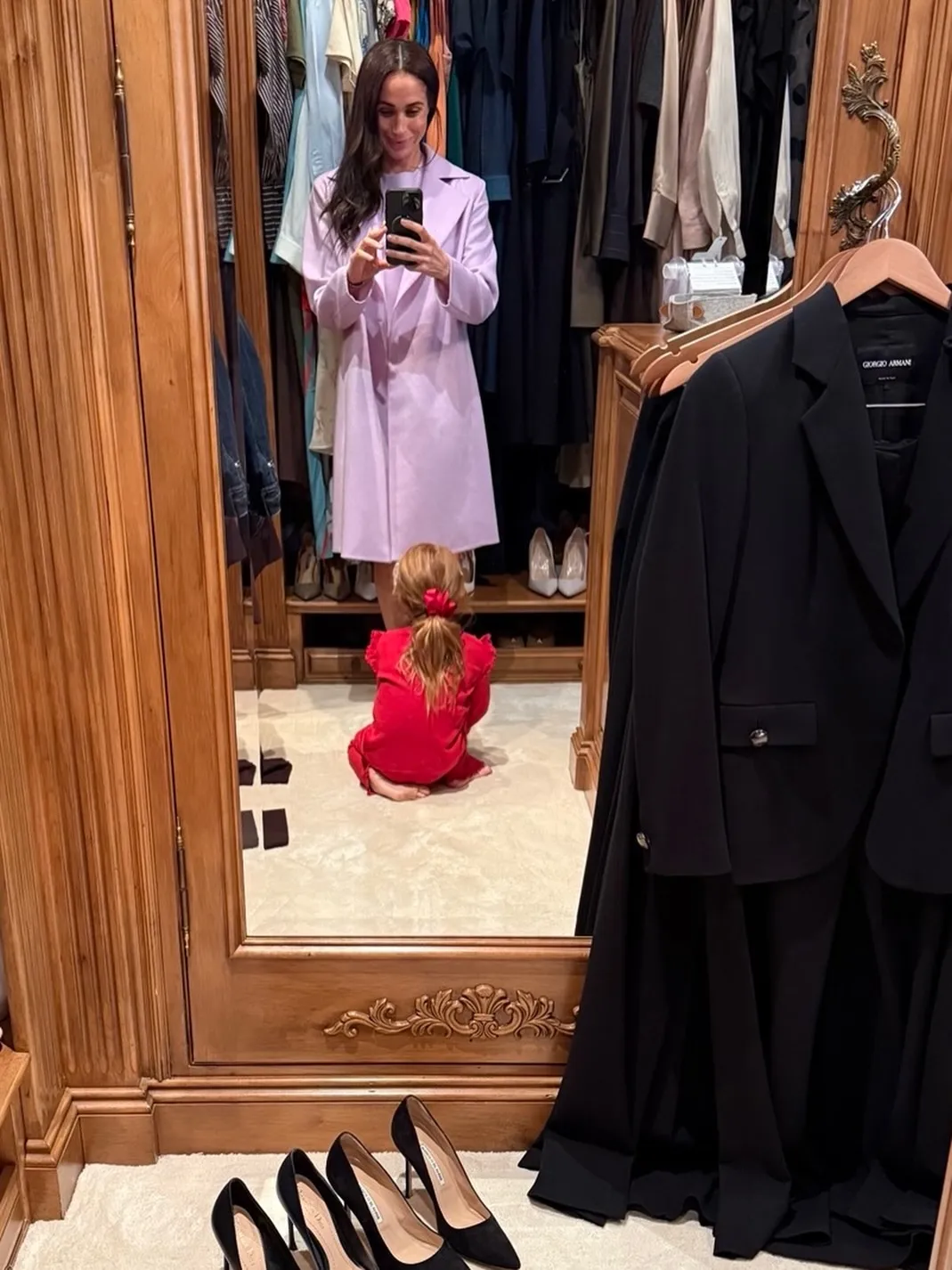 Meghan Markle taking a mirror selfie in her closet, with daughter Lilibet seated on the floor in front of her.