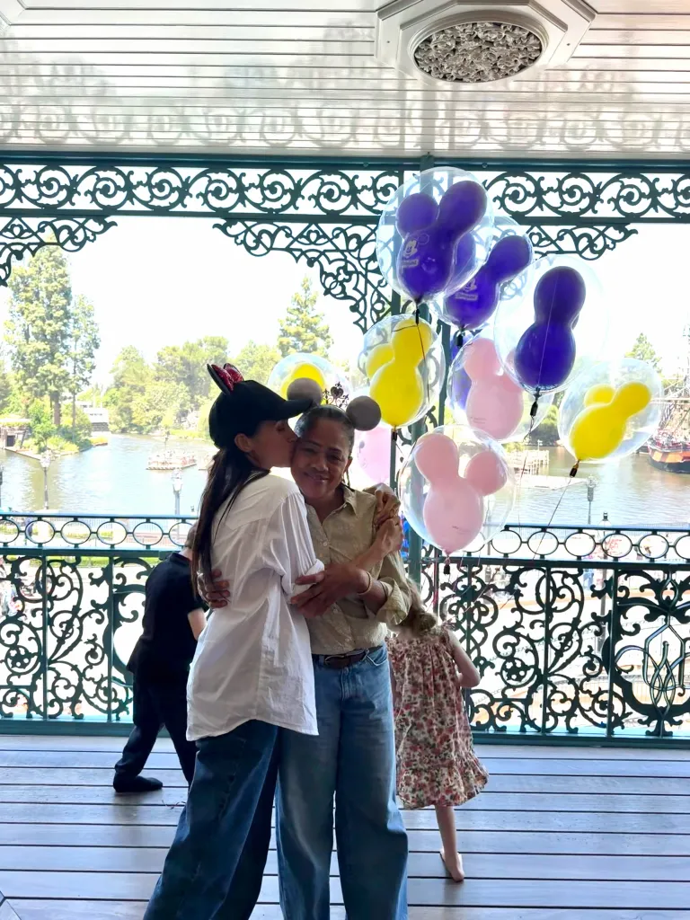 Woman in Minnie Mouse ears kissing another woman's cheek at Disneyland.