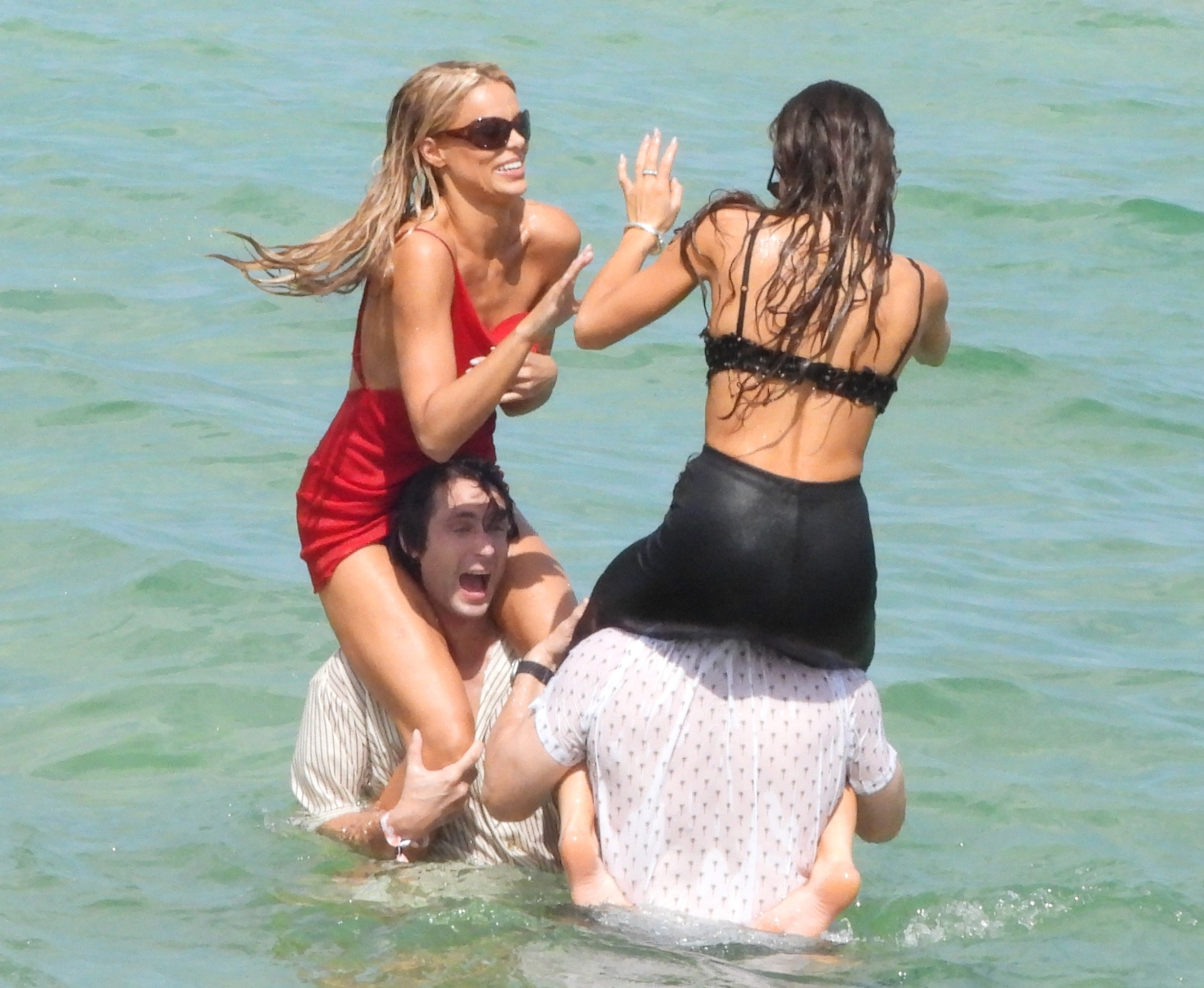 Brooks Nader and a sister riding on men's shoulders in the water, filming for their reality series.