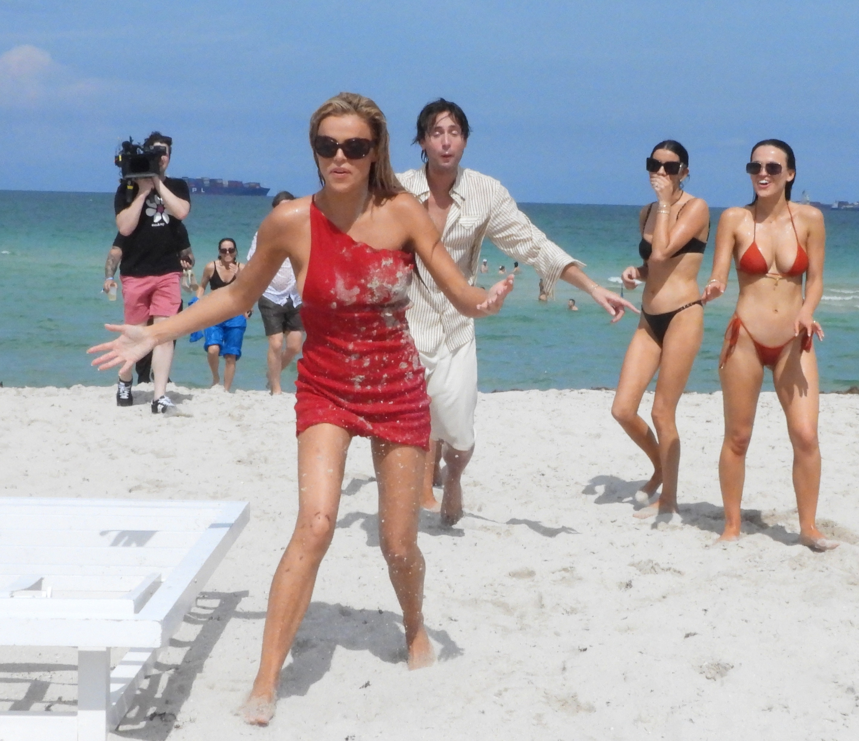 Brooks Nader in a red dress covered in sand, with two other women in bikinis behind her at Miami Swim Week 2026.