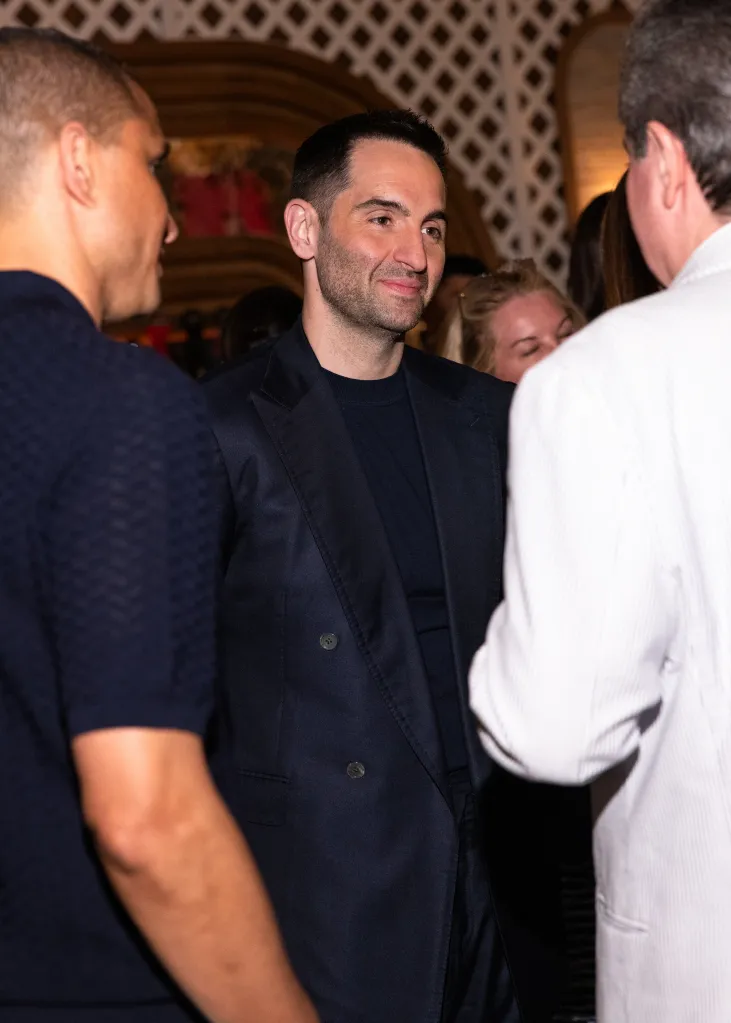 Mario Carbone smiles, wearing a dark blue suit and sweater, at the Bloomberg House Miami 2026 Opening Night VIP Dinner.