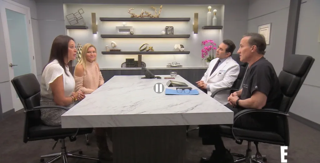 Two women and two doctors are seated at a marble conference table, discussing a medical issue.