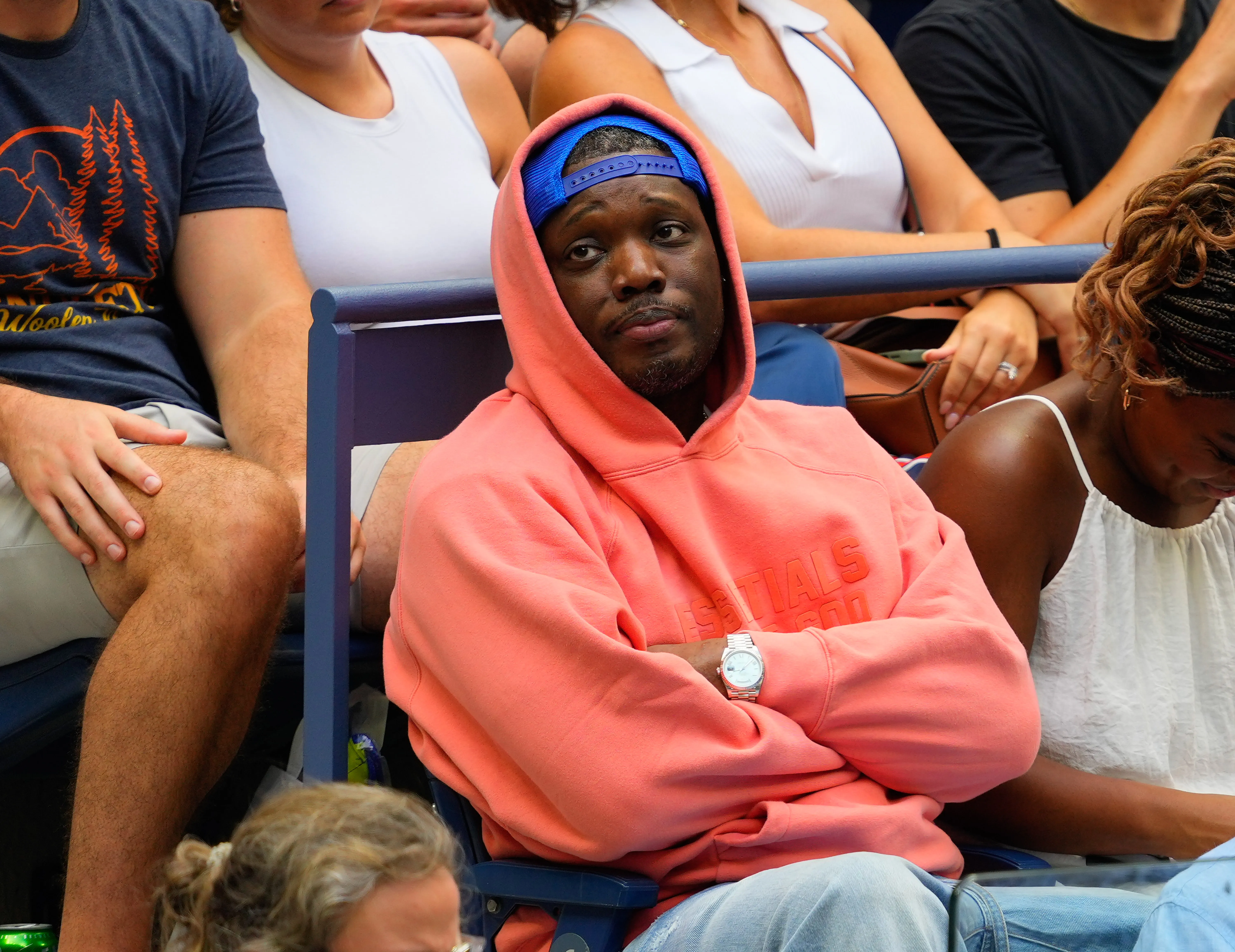 Michael Che in a coral hoodie and blue baseball cap attends the US Open Tennis Championships.