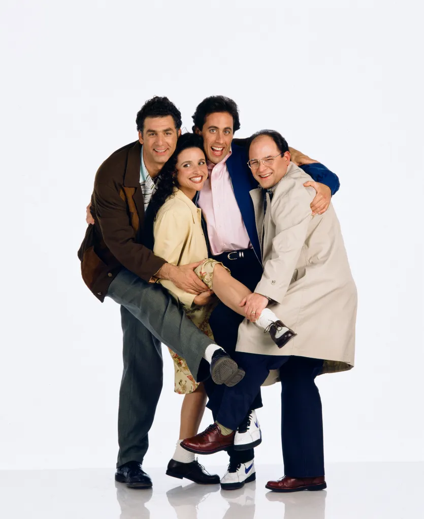 The cast of Seinfeld, including Michael Richards, Julia Louis-Dreyfus, Jerry Seinfeld, and Jason Alexander, smiling and embracing each other.