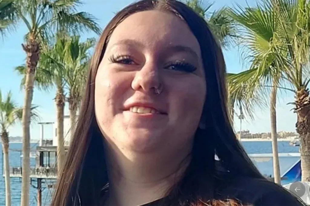 Photo of a young woman with long dark hair smiling in front of palm trees and ocean.