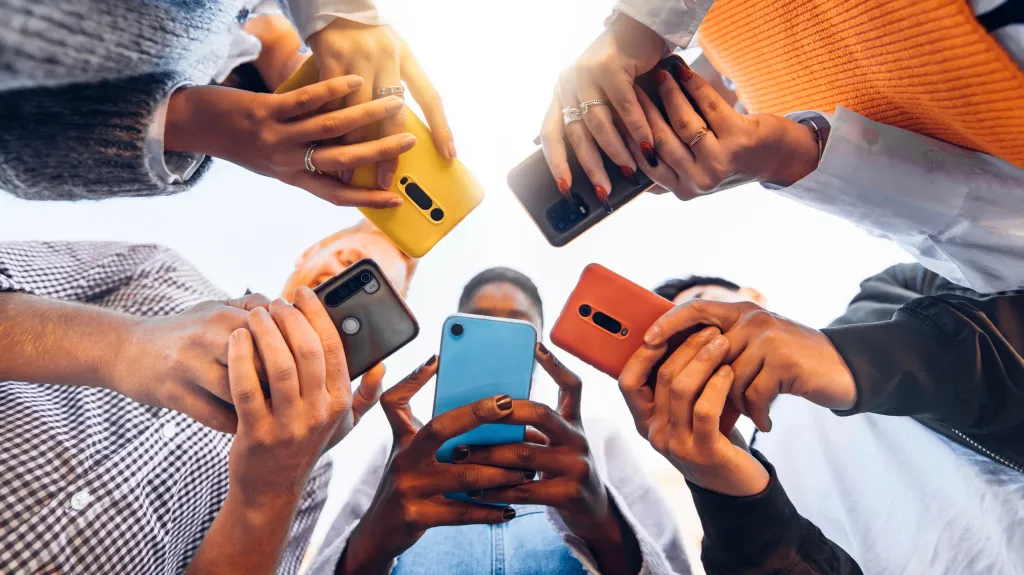 A low-angle view of six young people looking down at their cell phones in a circle.