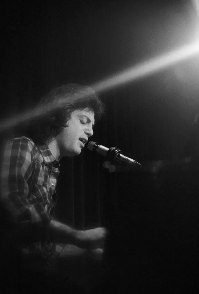 Billy Joel singing into a microphone on stage.