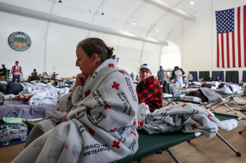 Natalie Bouriche sits on a cot in an evacuation center, wrapped in a Red Cross blanket, with her son behind her.