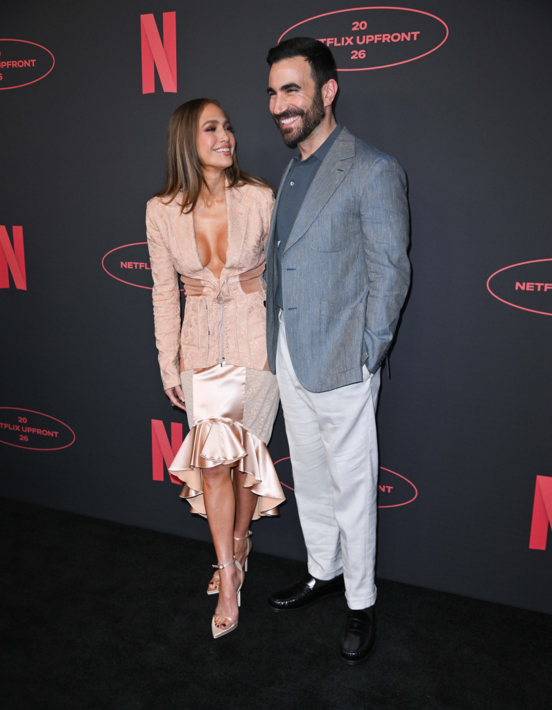 Jennifer Lopez and Brett Goldstein smiling at each other at the 2026 Netflix Upfront Presentation.