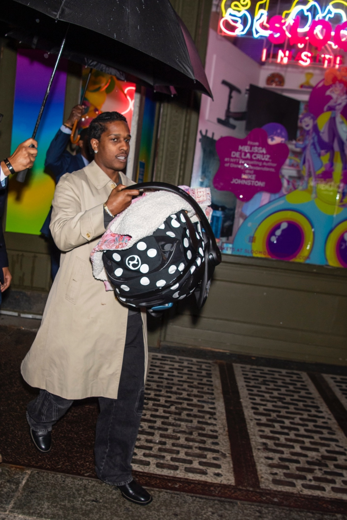 A$AP Rocky carrying a child car seat under an umbrella.