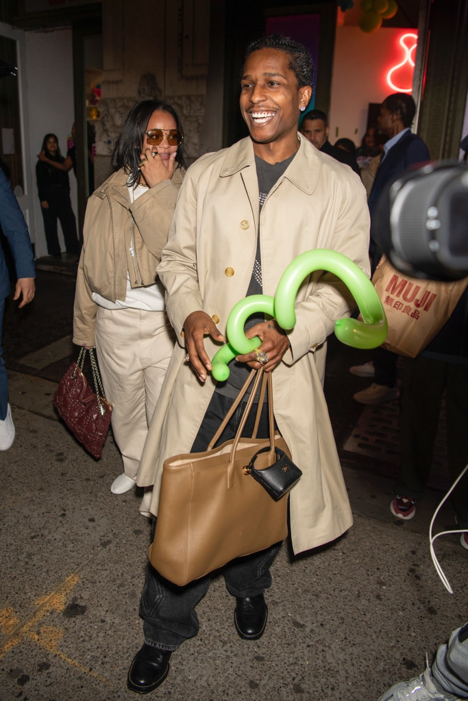 Rihanna and A$AP Rocky smiling, with A$AP Rocky holding a green balloon animal and a brown bag.