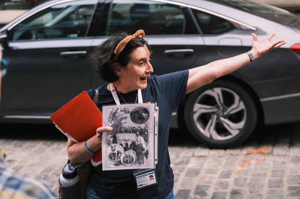Suzanne Reisman leading a tour of lower Manhattan, holding up an illustration of historical scenes.