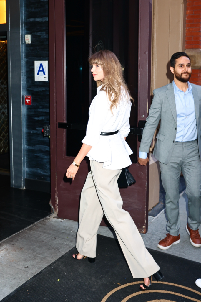 Taylor Swift arriving at Zero Bond in New York City wearing a white belted blouse, wide-leg trousers, and black heels.