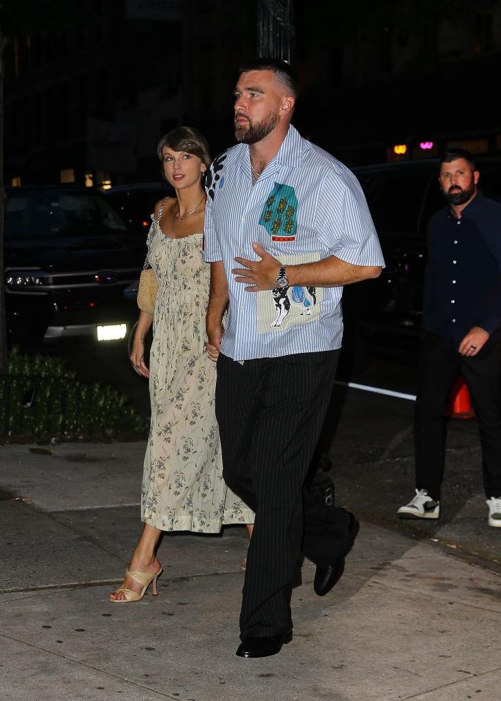 Taylor Swift and Travis Kelce holding hands while walking on a street at night.