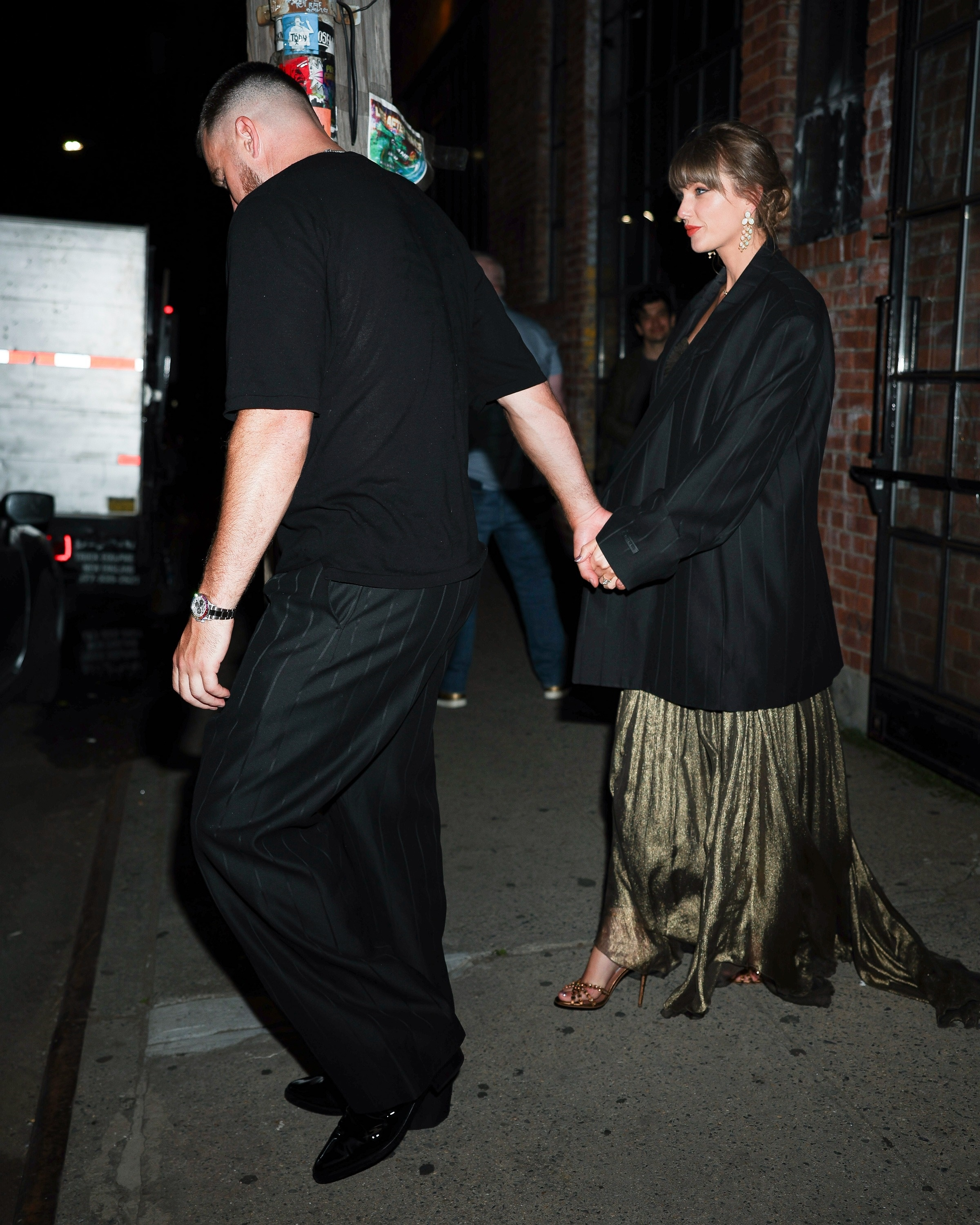 Taylor Swift and Travis Kelce holding hands, with Swift wearing Kelce's oversized jacket.