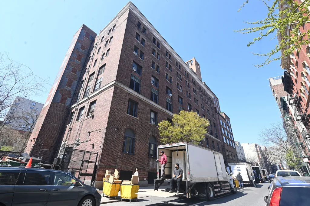 Workers load and unload materials from a truck outside a multi-story brick building.