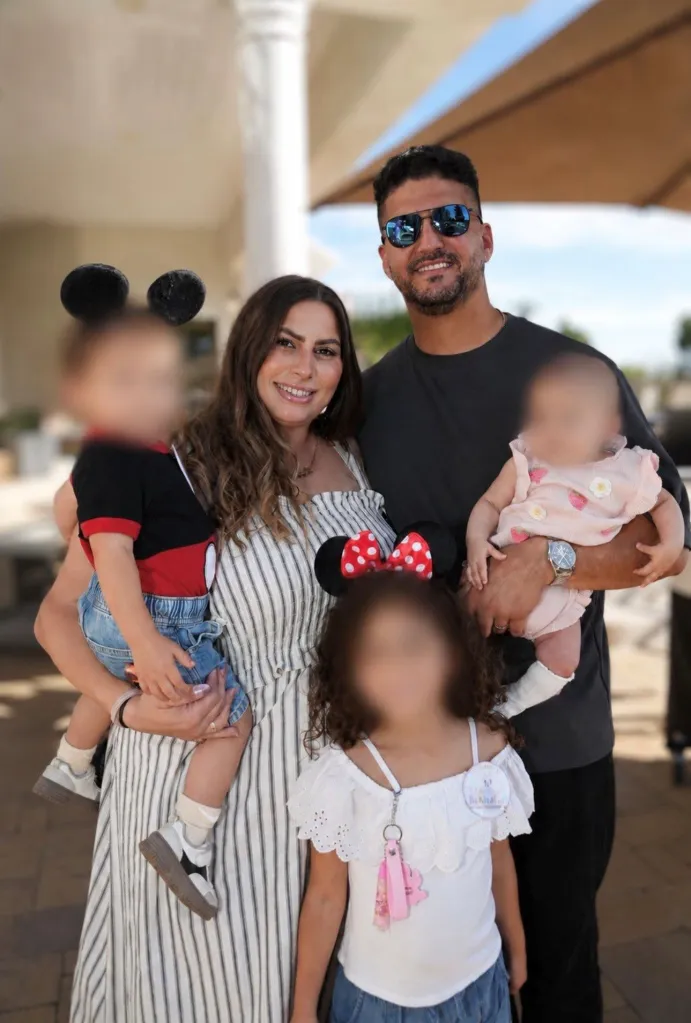 A smiling couple holds their three young children.