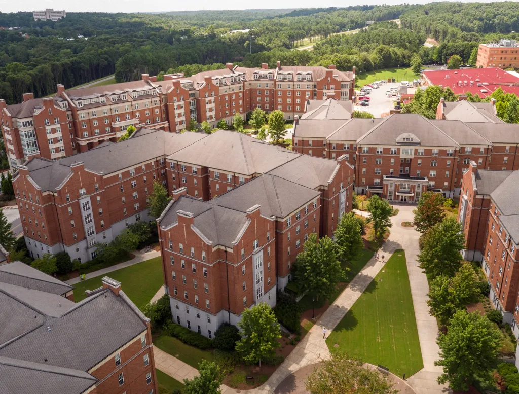Aerial view of the University of Georgia campus, showing several large, brick buildings with dark roofs, green lawns, and trees.