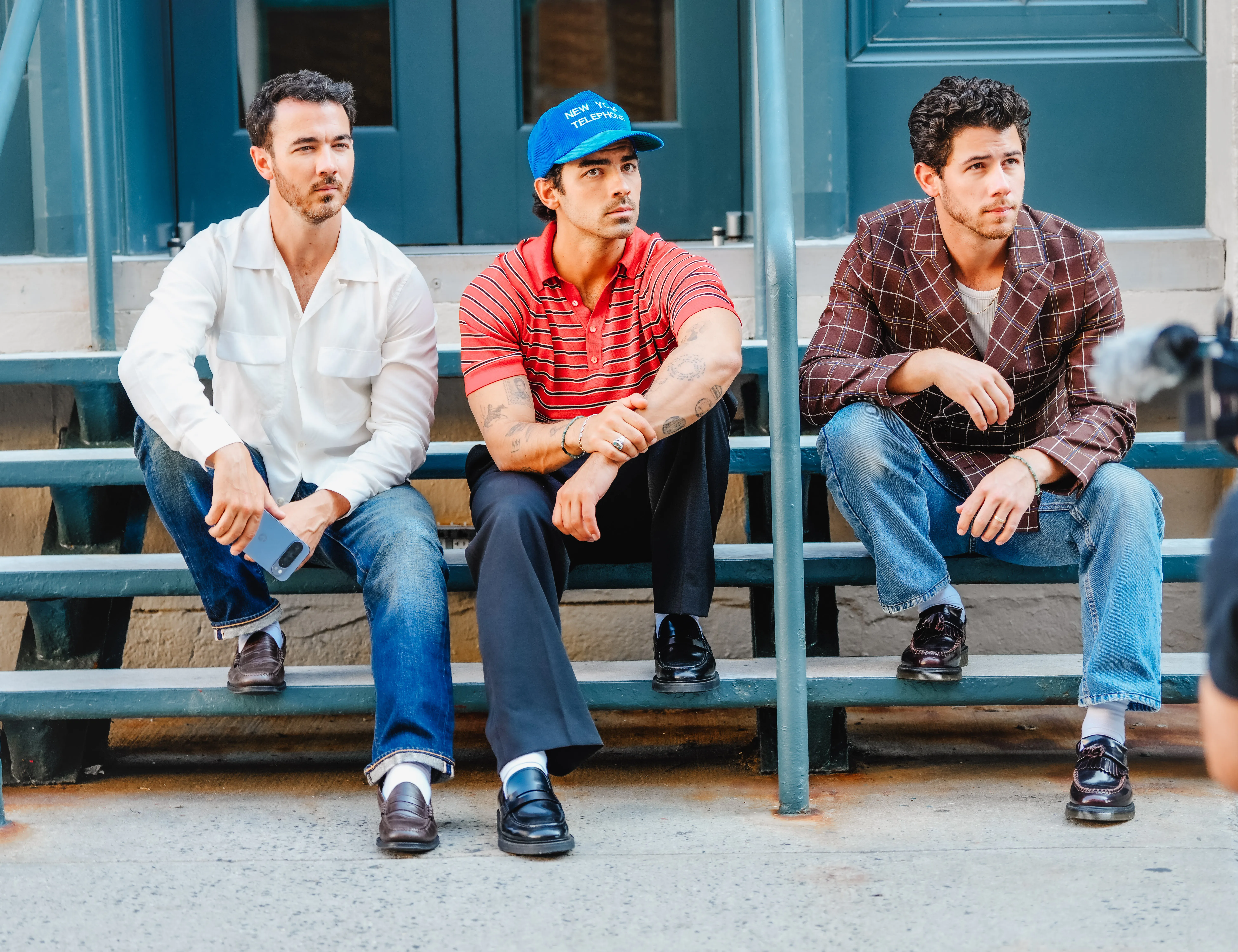 Kevin, Joe, and Nick Jonas sitting on blue metal steps.