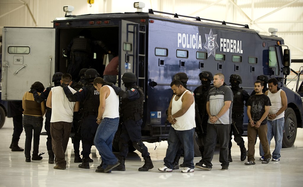 Alleged drug traffickers, handcuffed, are escorted by armed federal police officers towards and into a dark blue police truck.