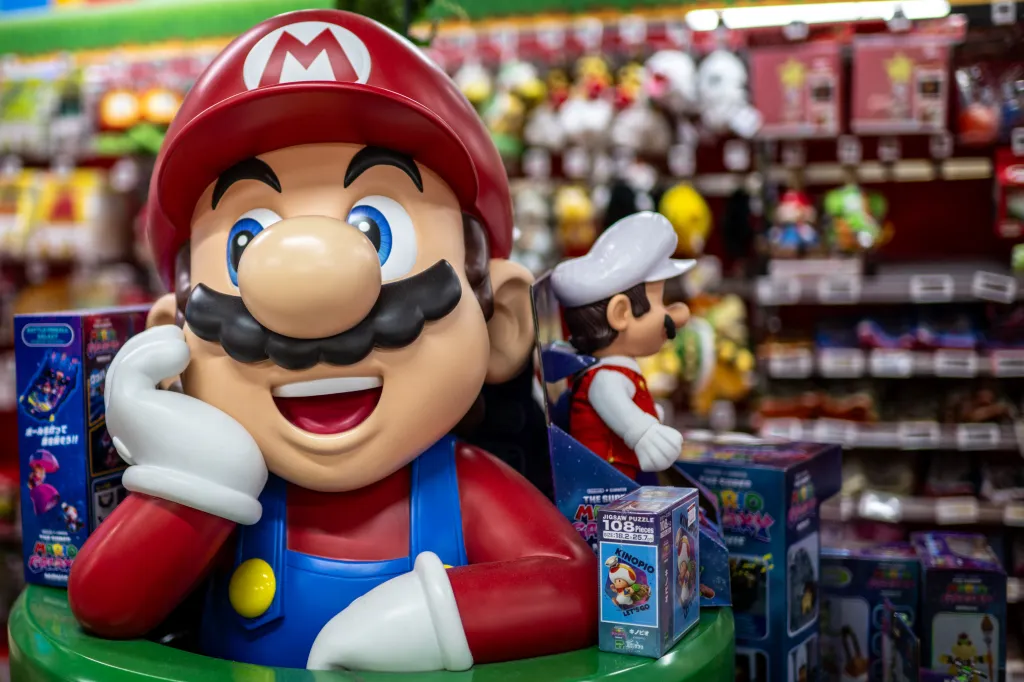 A large Mario figure and a smaller Luigi figure on display at a Nintendo store, with video games and plush toys visible in the background.