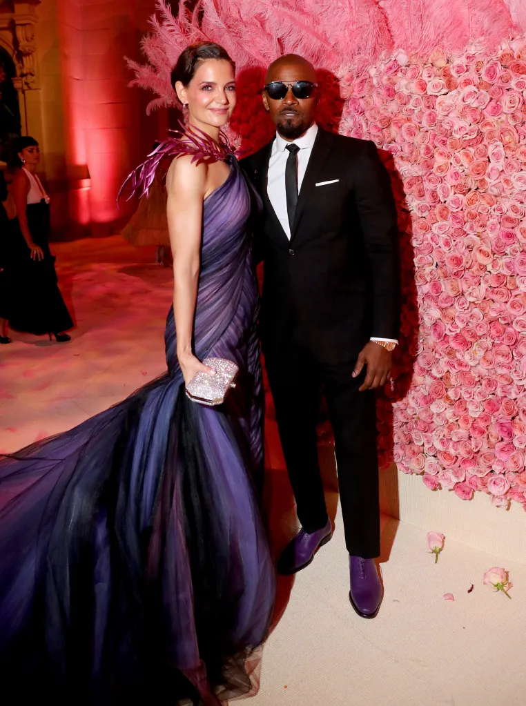 Katie Holmes in a purple ruffled gown and Jamie Foxx in a black suit with purple shoes, both smiling.