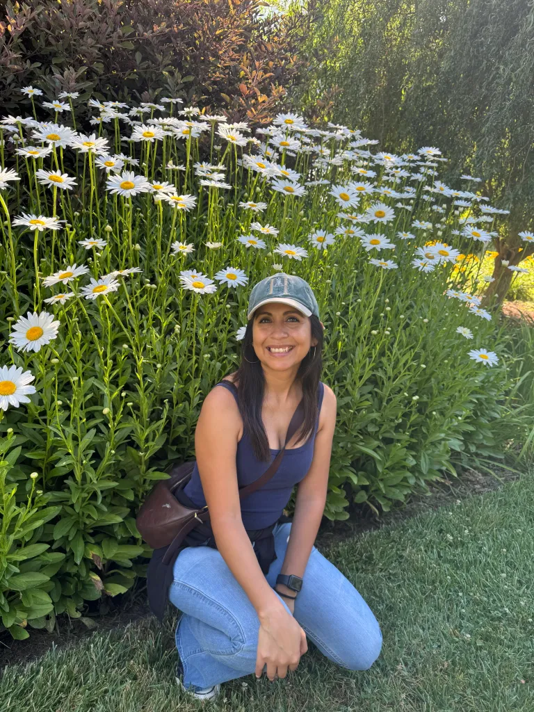 Shaina Montiel smiling while crouching in front of a field of white daisies.
