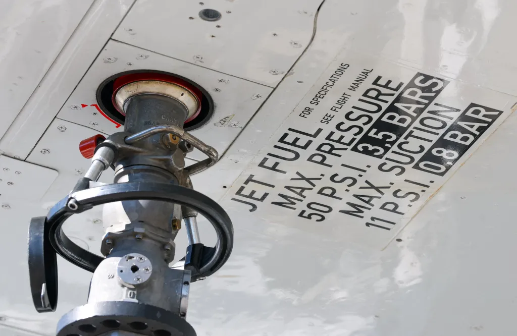 A nozzle attached under an aircraft wing for jet fuel refueling at an airport.