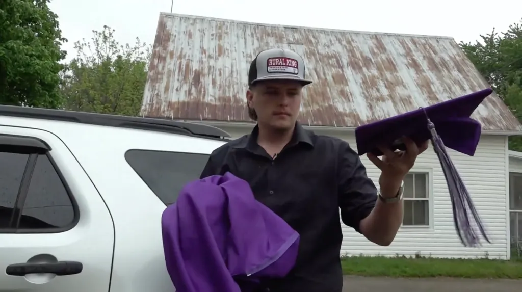 Alex Anderson holds up his regalia in front of his car after being barred from walking at the East Knox High School graduation on May 17, 2026.