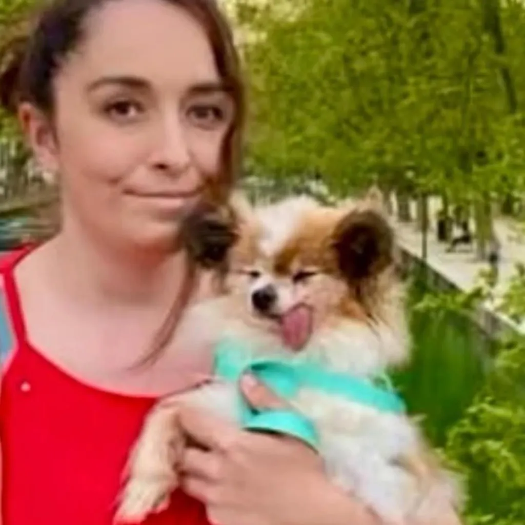 Woman holding a small dog with its tongue out.