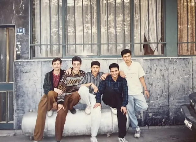 Five young men posing for a photo on a street.