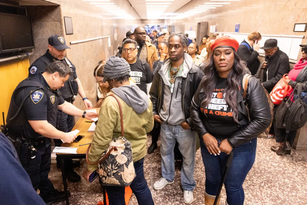 People attending the Carmella Charrington deed theft case in Brooklyn, NY, hand over their phones to officers.
