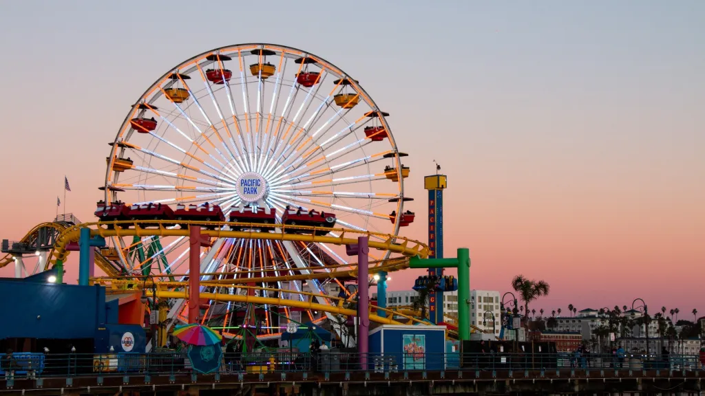 Pacific Park on the Santa Monica Pier with the Ferris Wheel and Route 66 West Coaster Roller Coaster at dusk.