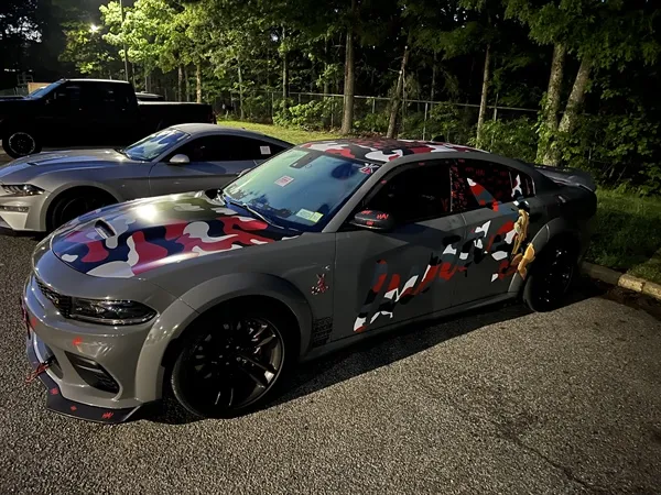 Two muscle cars, one with red, white, and gray camouflage, parked on asphalt.