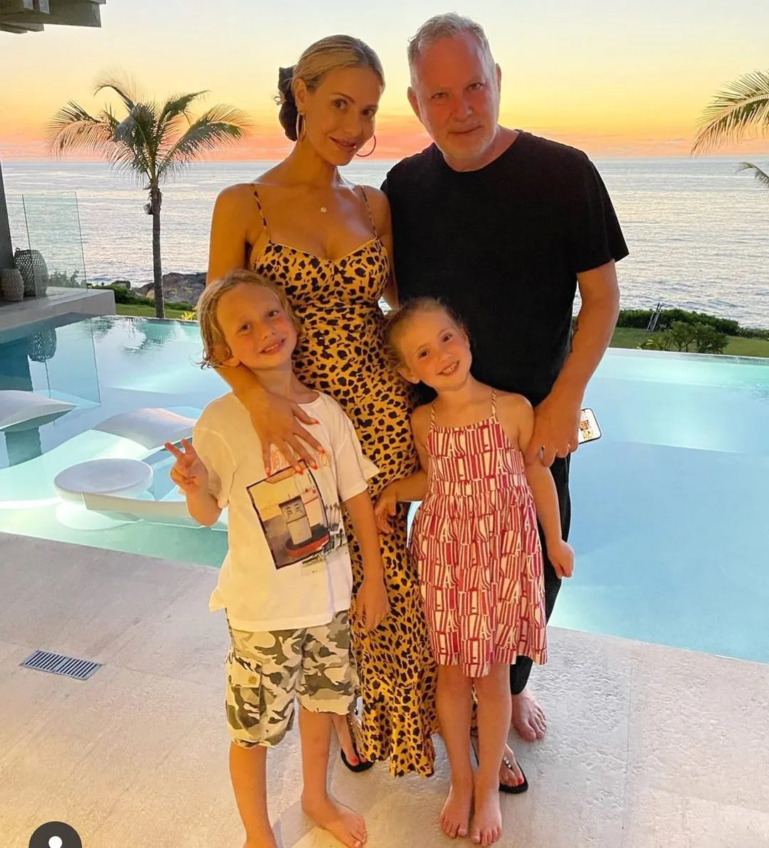 Paul Kemsley, Dorit Kemsley, and their two children smiling for a photo outside a home overlooking the ocean at sunset.